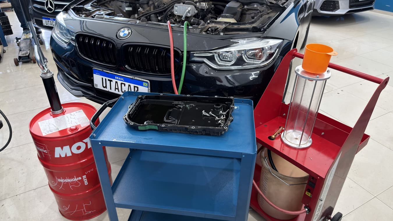Cárter do câmbio automático removido sobre o carrinho, com os parafusos sobre a peça, entre o barril de fluido e a máquina de troca.