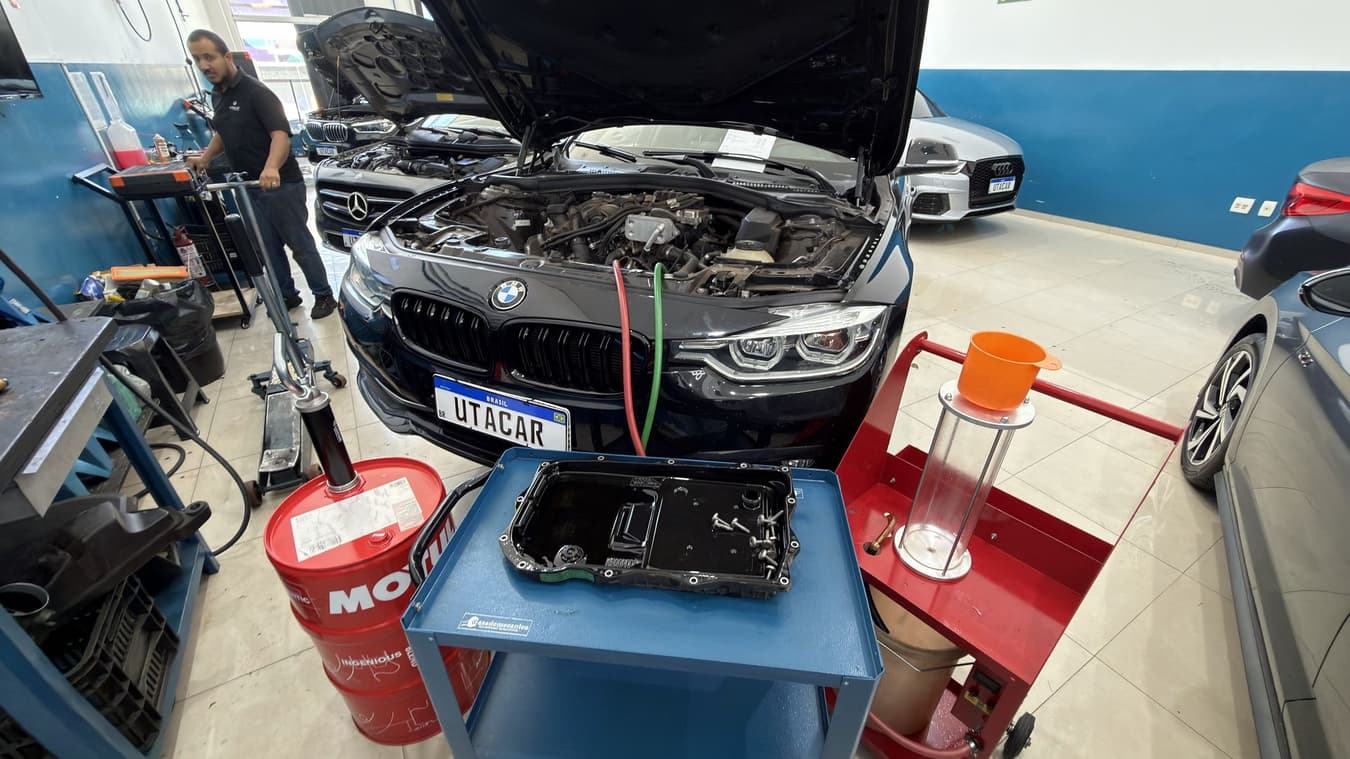 Vista aberta da oficina da Utacar durante o serviço: o carro conectado à máquina de troca de fluido e um técnico da equipe ao fundo.