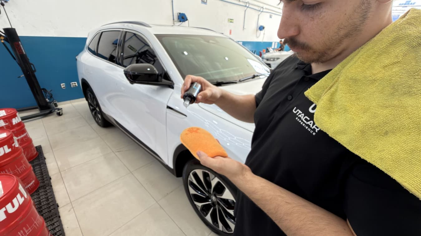 Técnico da Utacar com o frasco de coating e o aplicador na mão, diante do SUV branco preparado no box de estética.