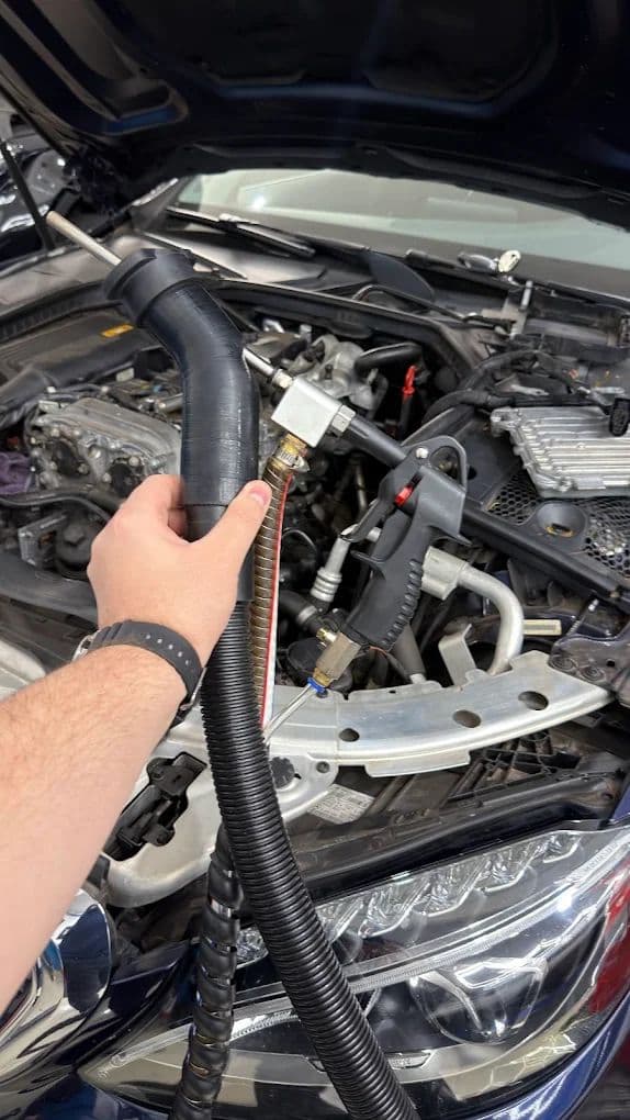 Mão do técnico posiciona o adaptador de sucção na admissão do motor durante a limpeza com casca de noz.