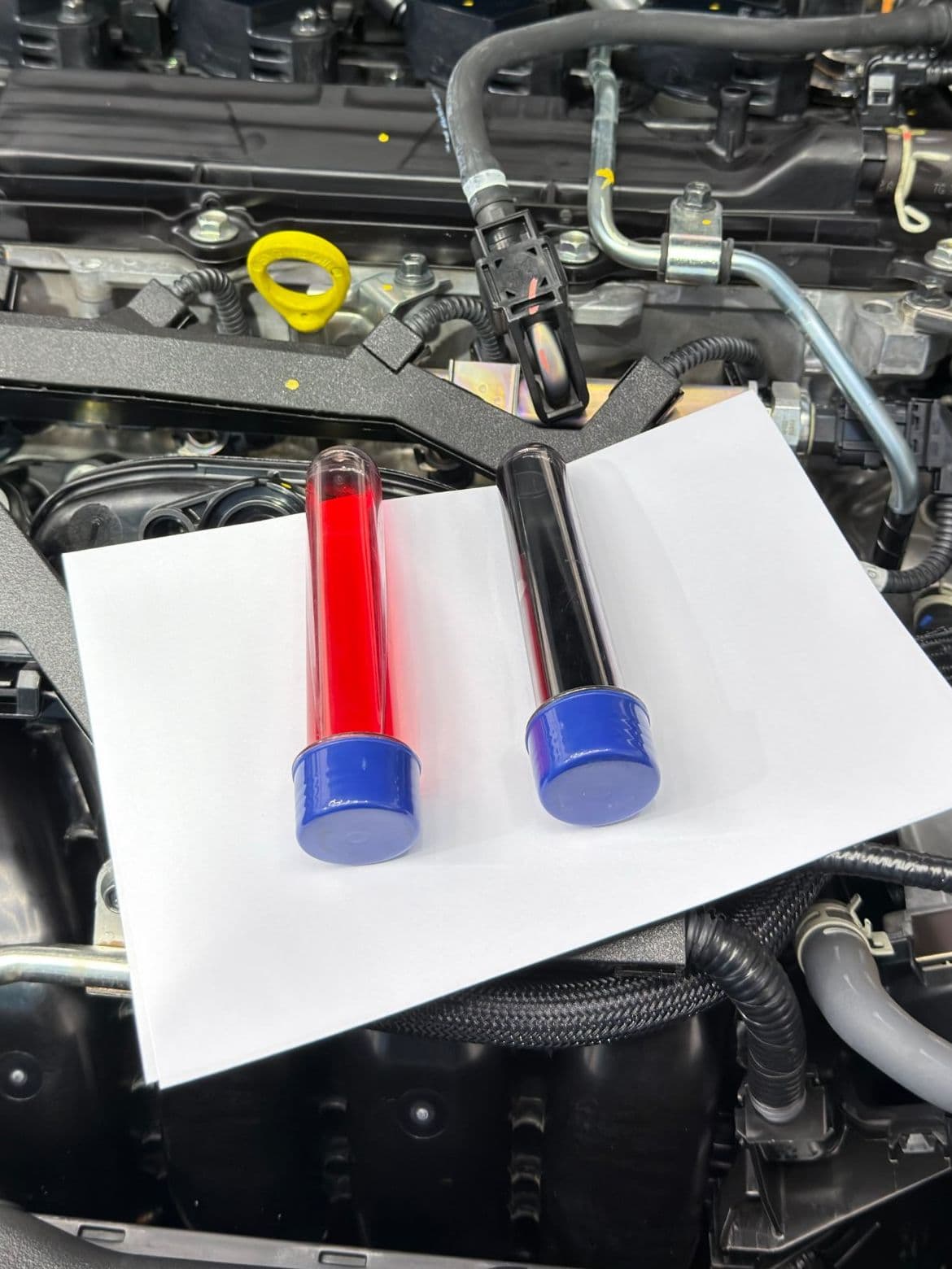 Duas amostras de fluido de câmbio automático lado a lado sobre papel branco no cofre do motor, uma vermelha e limpa e outra escurecida pelo uso