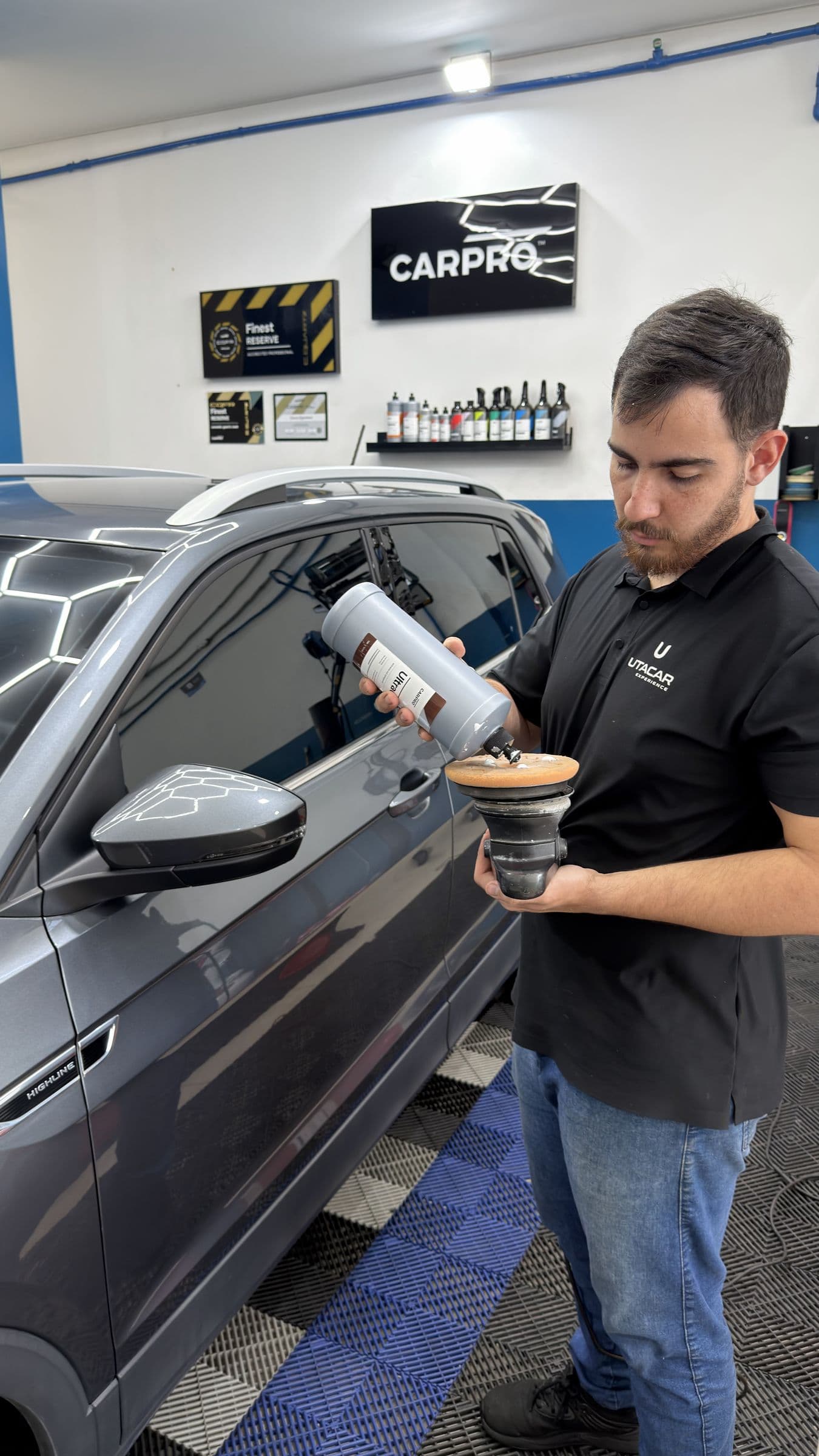 Profissional da equipe segurando a politriz com a boina de polimento, ao lado de um SUV cinza.