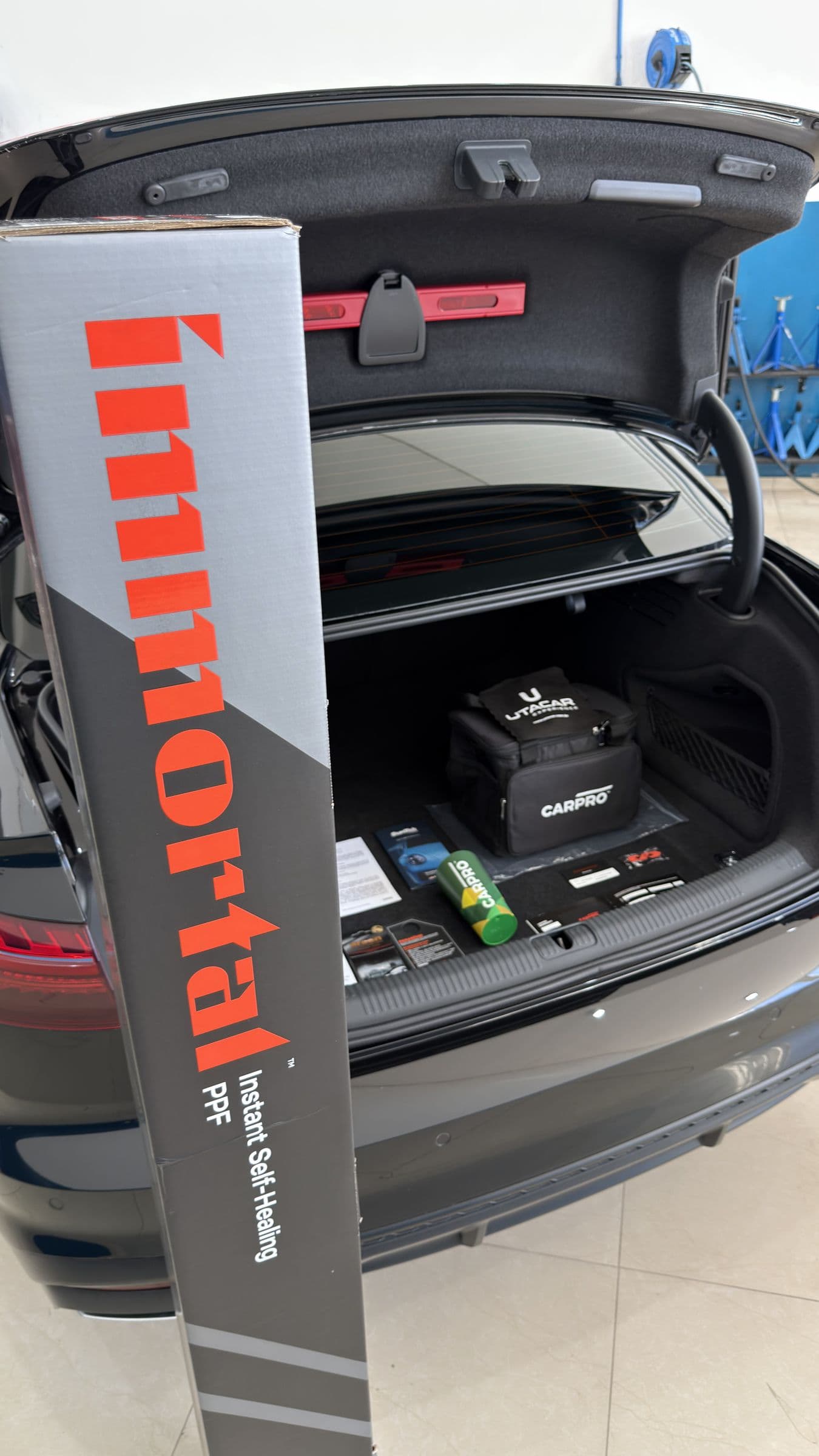 Caixa do PPF CARPRO Immortal apoiada no porta-malas aberto, com o kit de entrega da Utacar dentro.