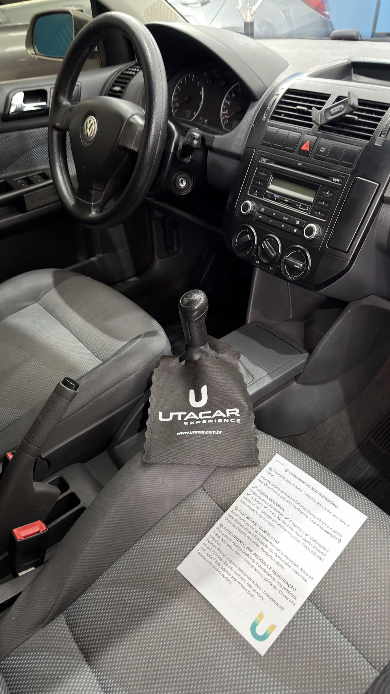 Interior de um Volkswagen pronto para a entrega, com a flanela UTACAR sobre o câmbio e o cartão de orientações apoiado no banco do carona.