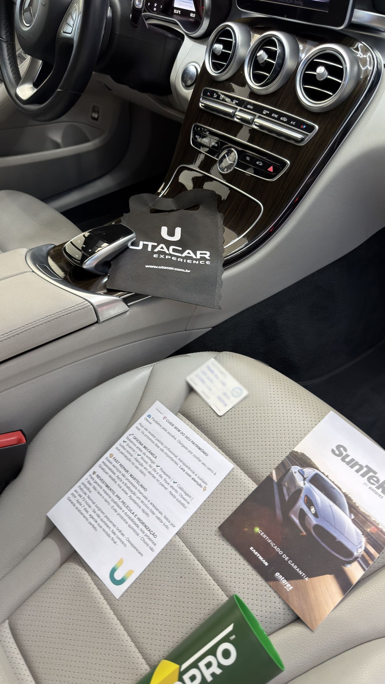 Interior claro de uma Mercedes-Benz pronta para a entrega, com a flanela UTACAR sobre o console, o cartão de orientações e o certificado de garantia SunTek no banco.