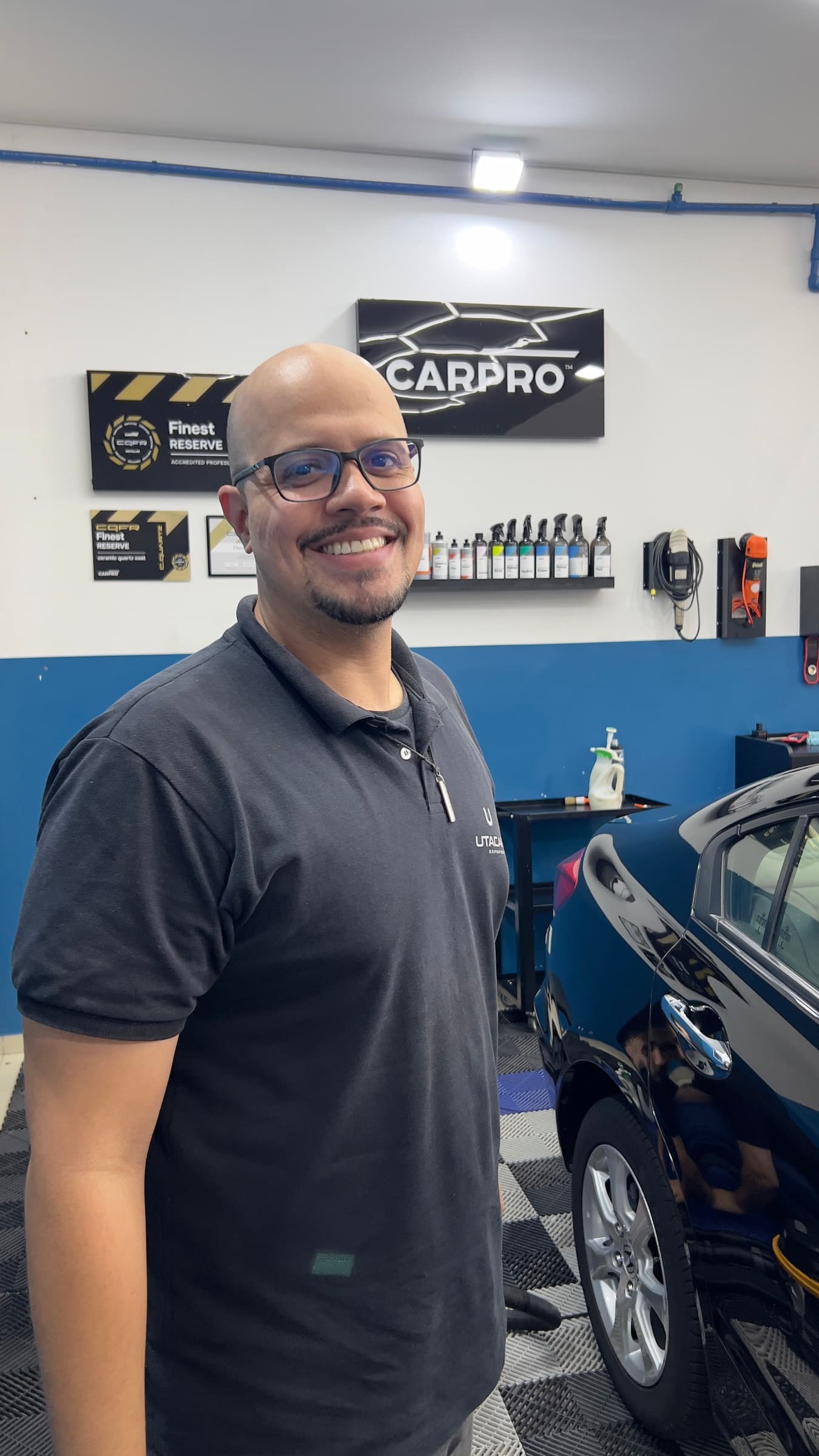 Bruno Ferreira, responsável pela oficina da Utacar, de uniforme, no box de estética com o painel da CARPRO ao fundo.