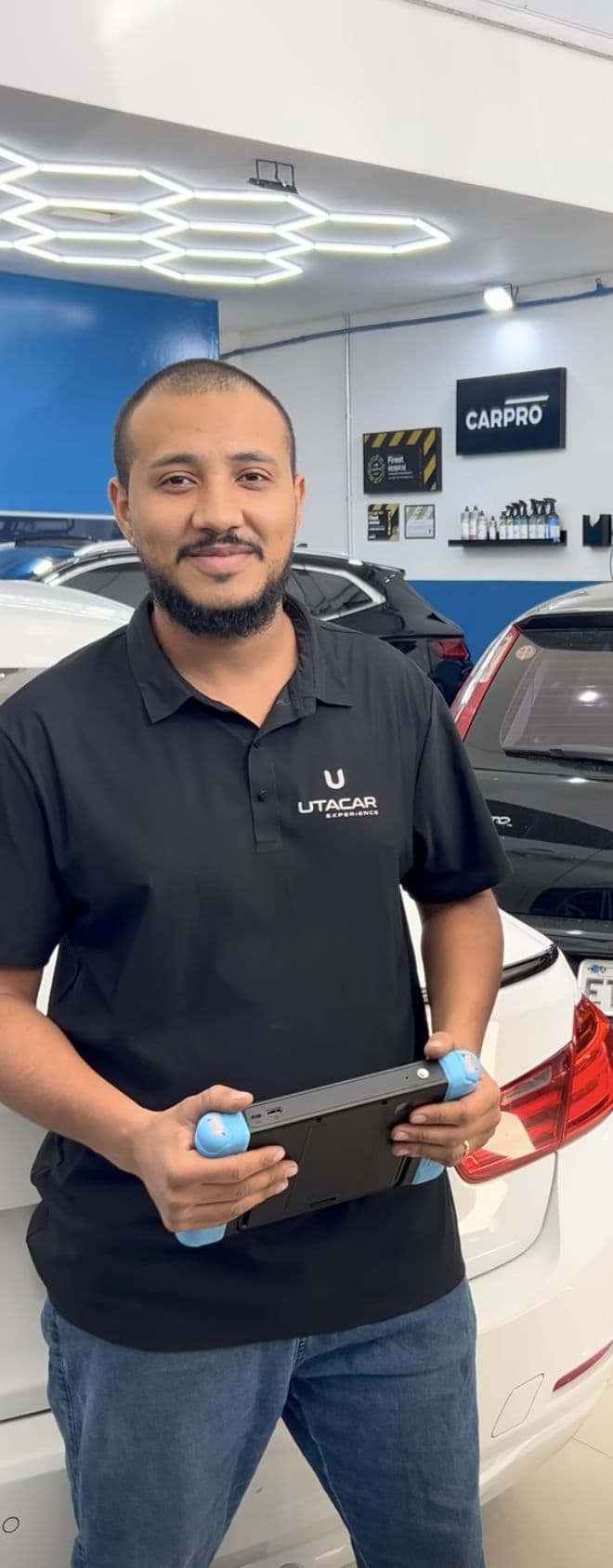 Kelvin Lima, técnico de oficina da Utacar, de uniforme e com o tablet de diagnóstico na mão, no salão da loja.