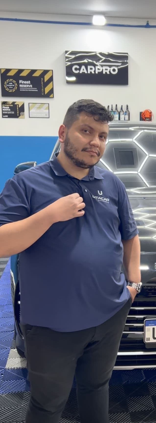 Rafael Lima, consultor técnico da Utacar, de uniforme, no salão da loja com o painel da CARPRO ao fundo.