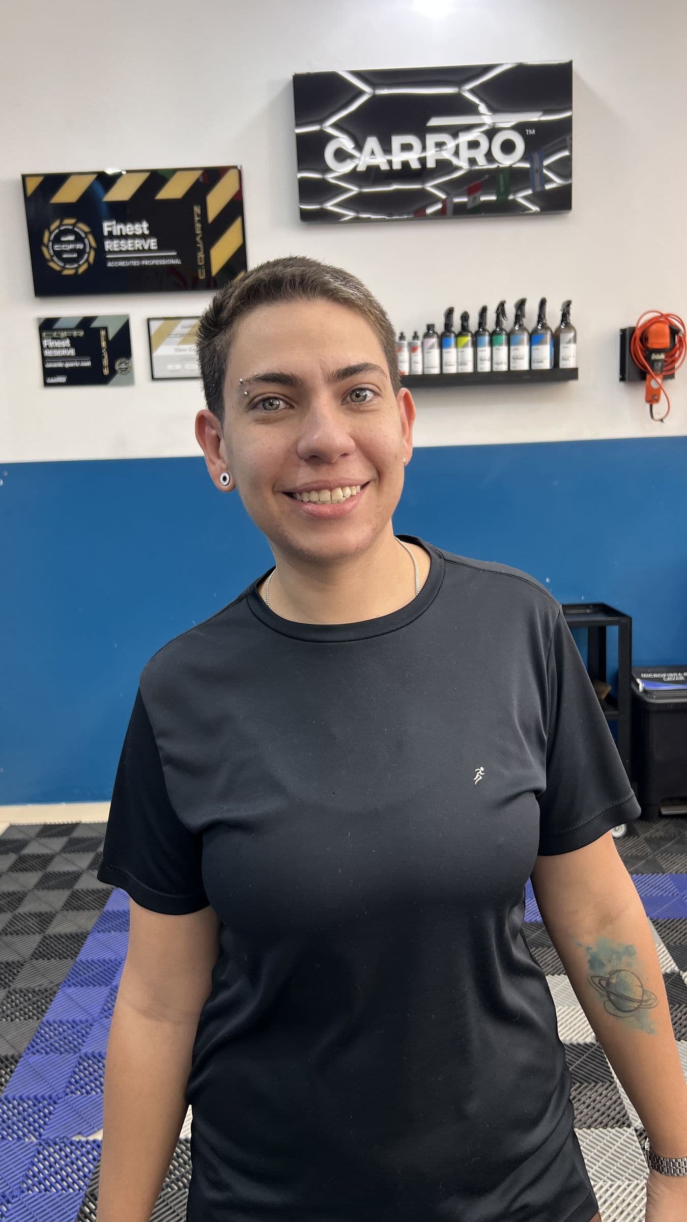Giovana Marucci, de marketing e relacionamento da Utacar, no salão da loja com o painel da CARPRO e o expositor de produtos ao fundo.