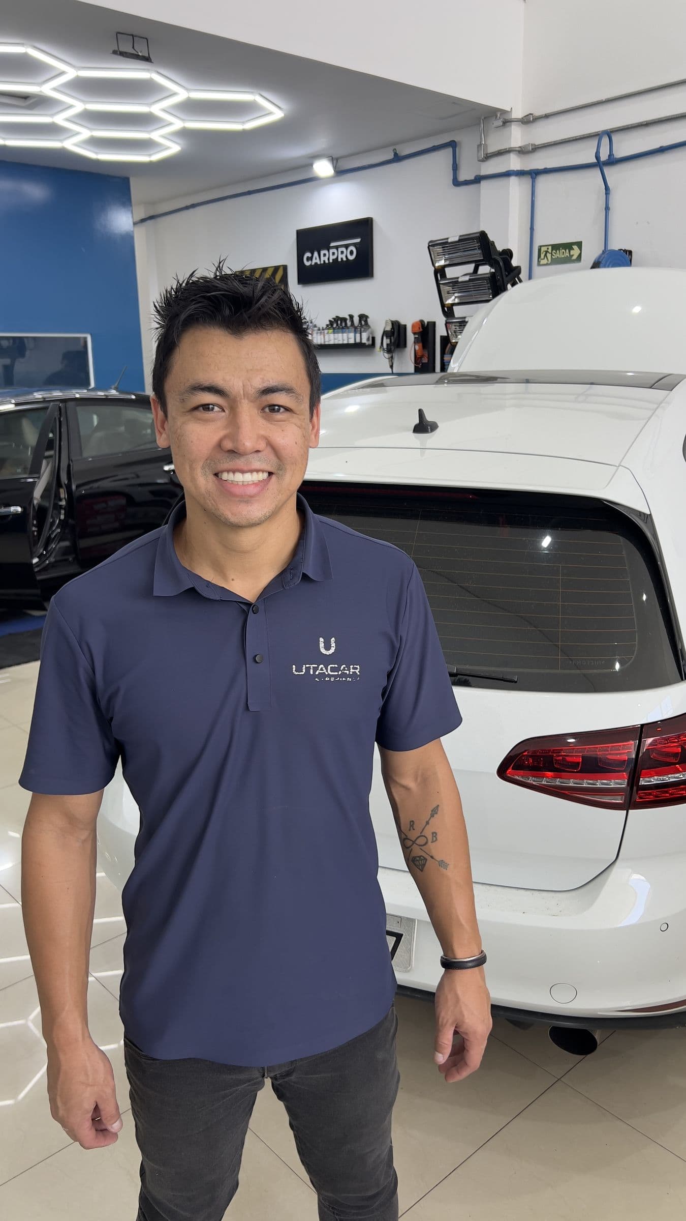 Renato Hidaka, responsável pelas operações da Utacar, de uniforme, ao lado de um Volkswagen branco no box de estética.