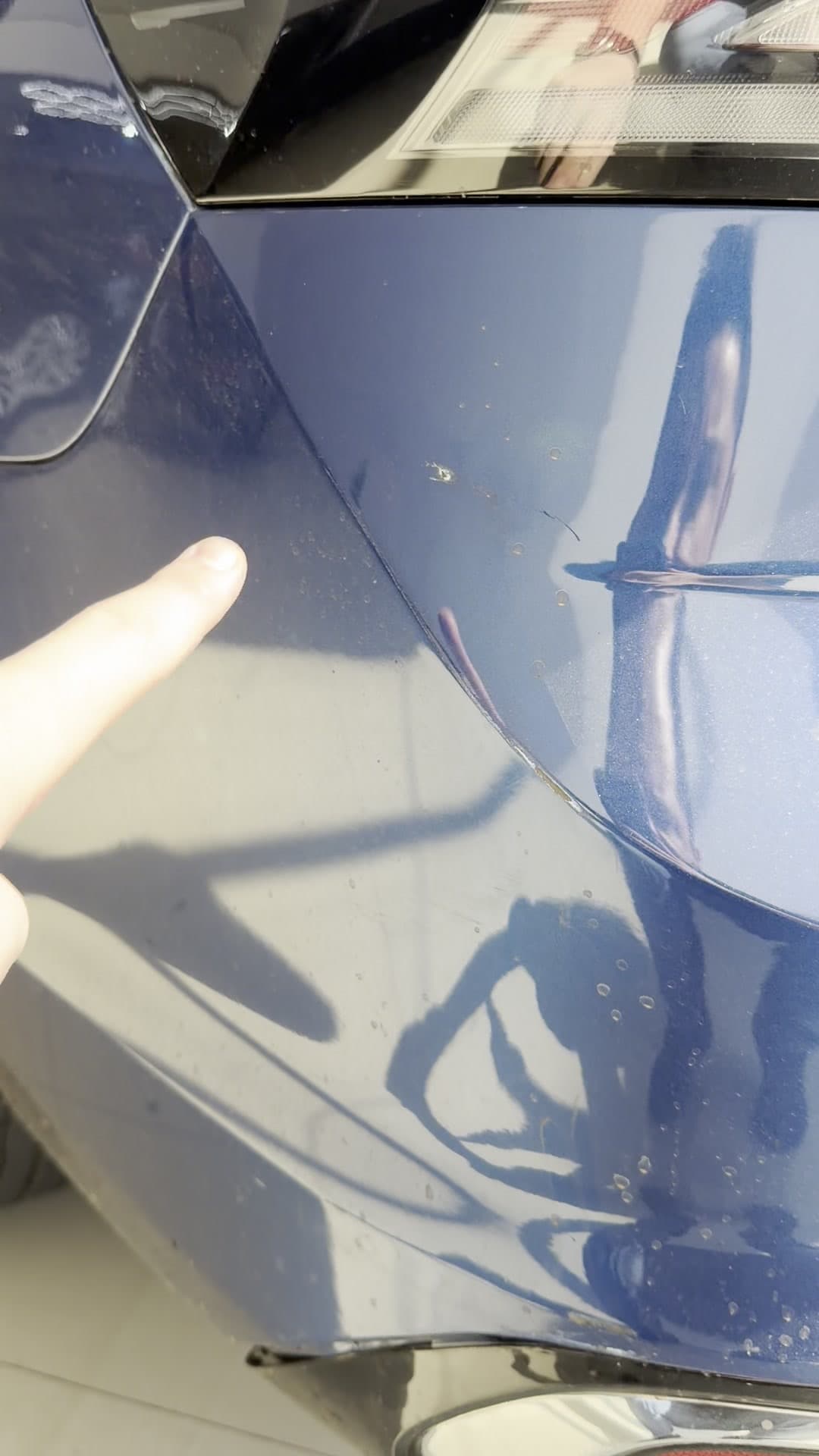 Detalhe do amassado na lataria, com o dedo indicando a extensão do defeito.