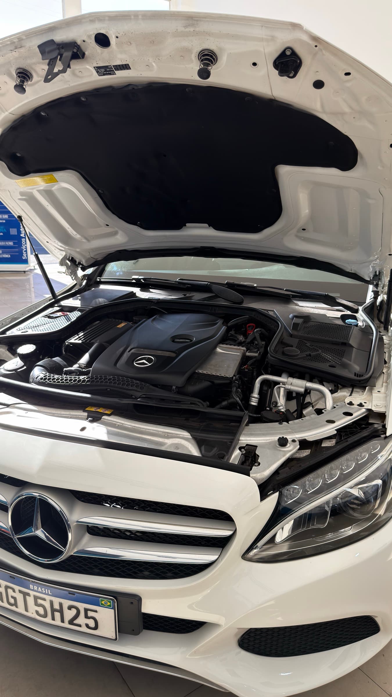 Capô aberto de um Mercedes branco dentro da oficina, com o motor à mostra.