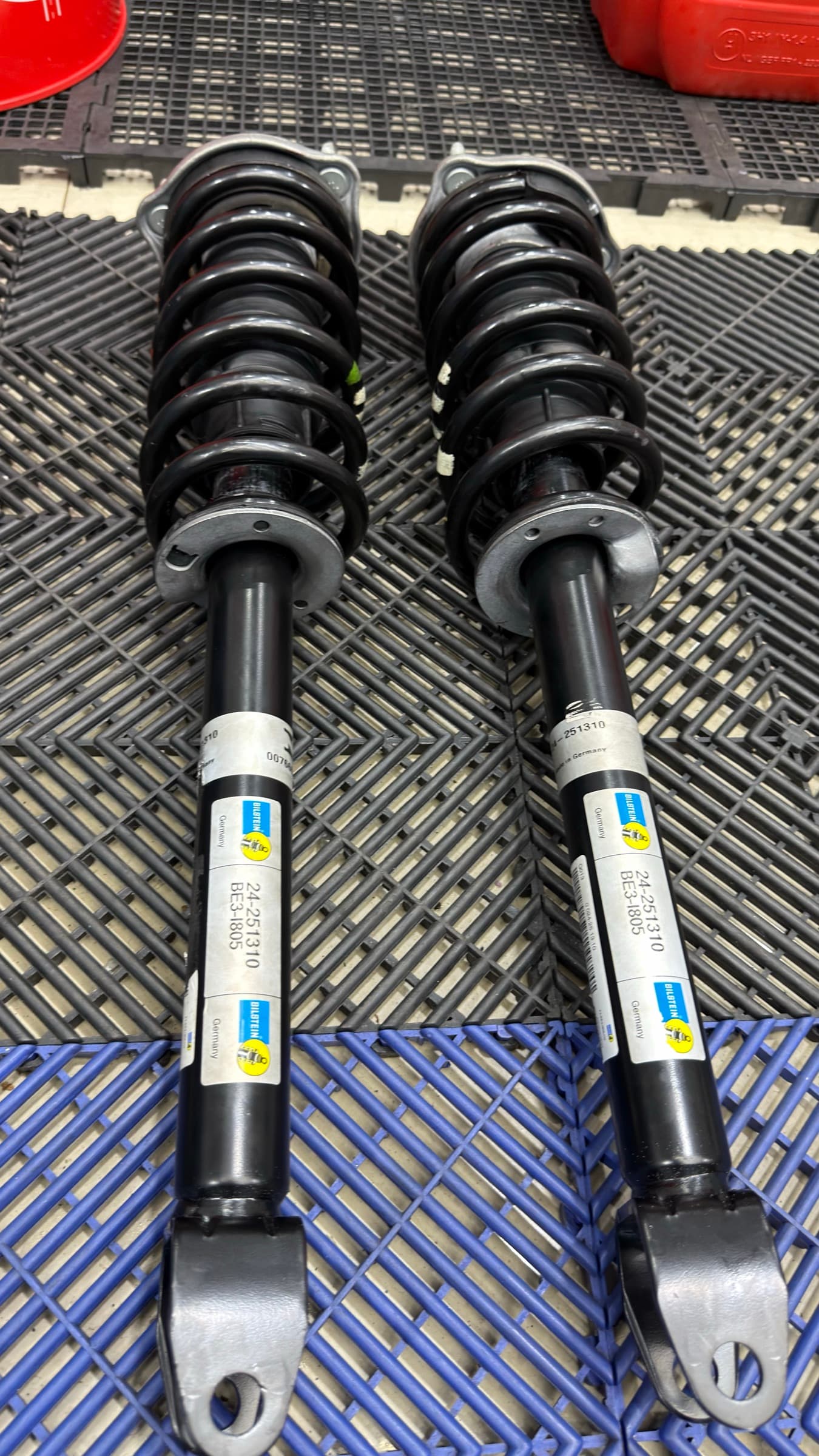 Par de amortecedores Bilstein novos, com as molas já montadas, apoiados no piso do box.