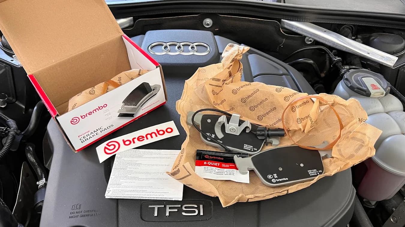 Pastilhas de freio Brembo novas sobre o motor de um Audi TFSI, ao lado das pastilhas usadas que saíram do carro.