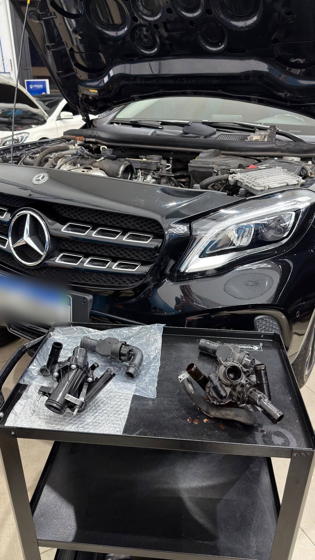 Mercedes-Benz GLA com o capô aberto e as peças do sistema de arrefecimento, usadas e novas, dispostas sobre o carrinho de ferramentas.
