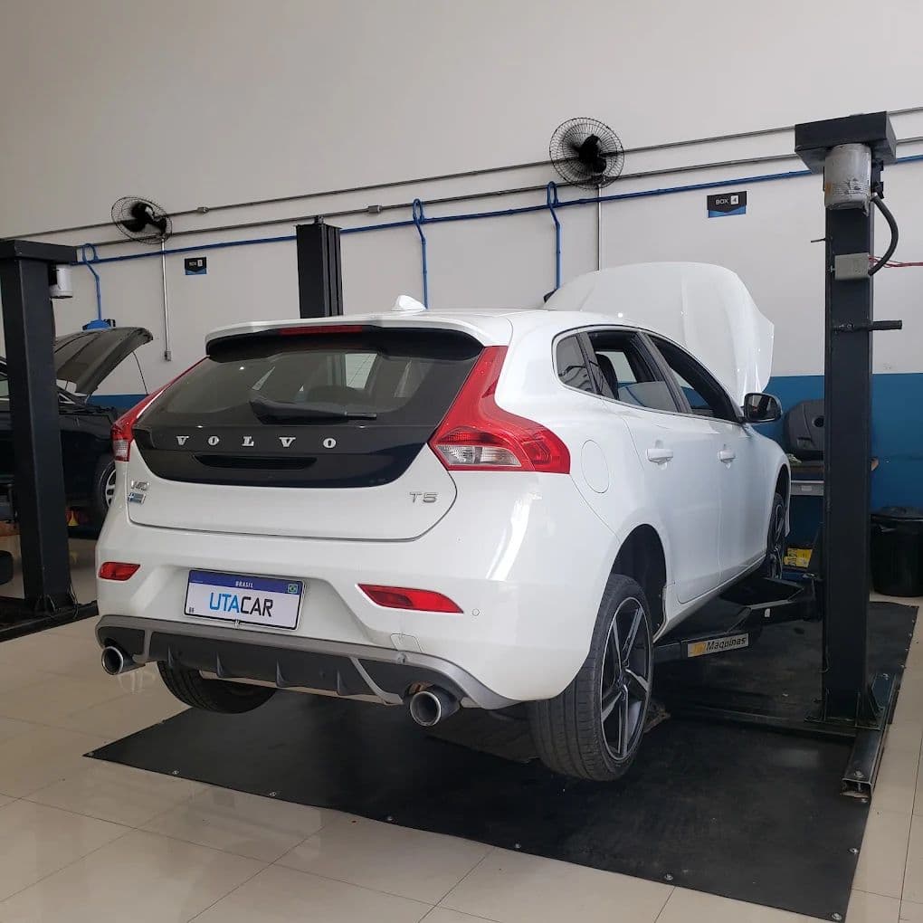 Volvo V40 branco visto de trás sobre o elevador de duas colunas, com a placa de cobertura da UTACAR.