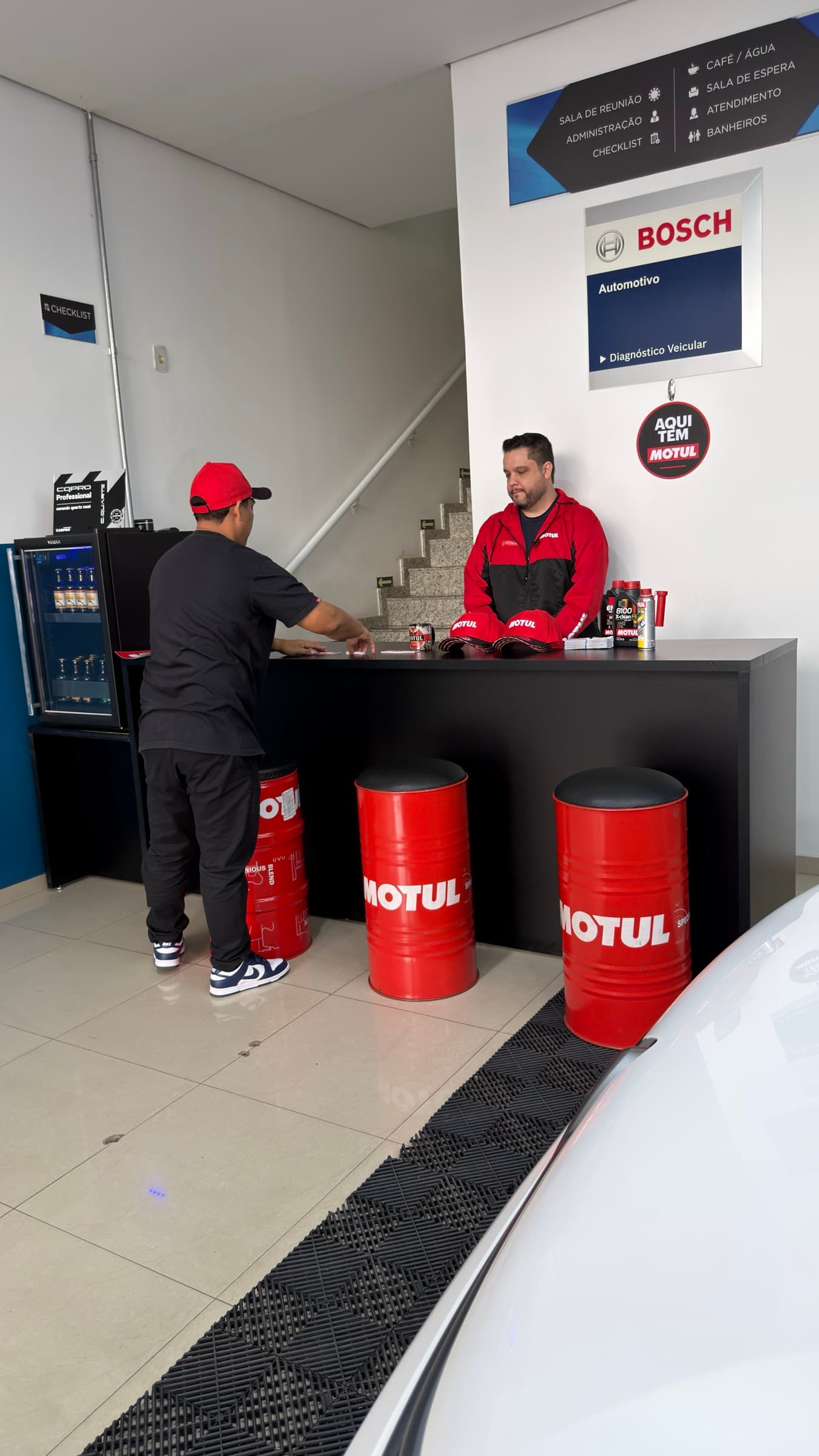 Balcão de atendimento da loja, com dois funcionários e os painéis da Bosch e da Motul ao fundo.