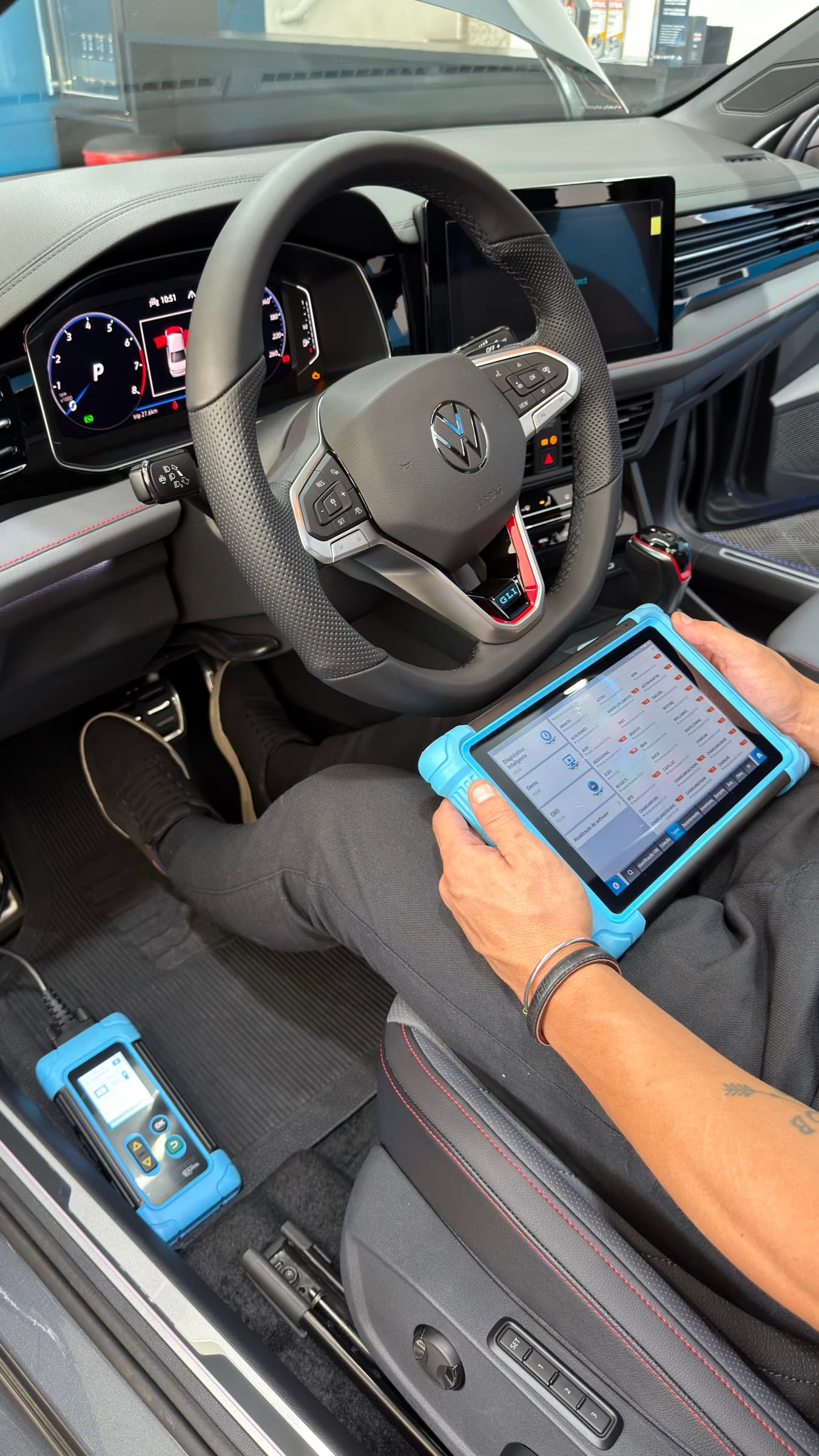 Técnico sentado no banco do motorista operando o tablet de diagnóstico conectado ao carro, com o painel do veículo aceso.