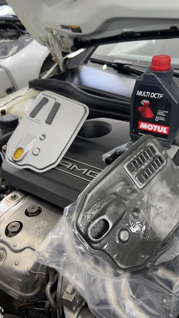 Filtro de transmissão novo e frasco de fluido Motul Multi DCTF apoiados sobre a tampa do motor, ao lado do cárter do câmbio recém-removido.